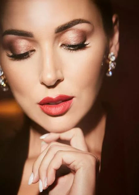 Макияж: ухаживающий тональный крем Intensive Serum Foundation SPF 40 (Natural); компактная пудра с эффектом загара Bronzing Powder (Natural); компактная пудра для придания сияния Highlighting Powder (Bronze Glow); устойчивые тени для век Long-Wear Cream Shadow Stick (Golden Bronze); матовая помада для губ Luxe Matte Lip Color (On Fire); карандаш для губ Lip Pencil (Red). Все — Bobbi Brown